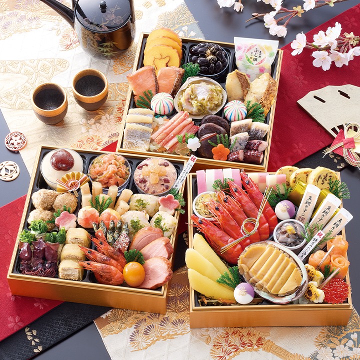 金色の三段重を3つ並べたおせち。海老、鮑、伊達巻、黒豆などが見える