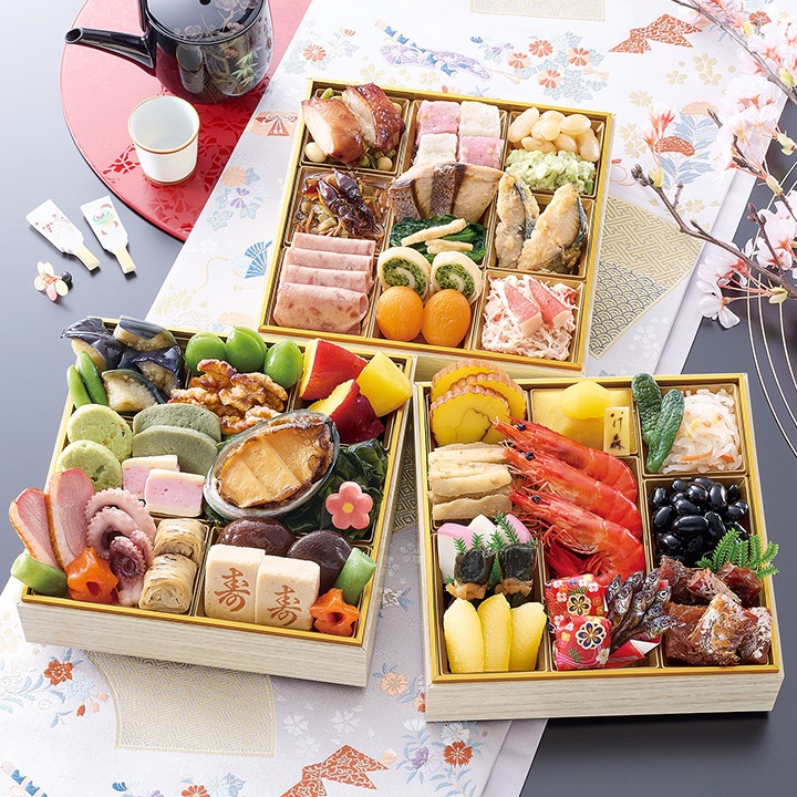 白木風の三段重を3つ並べたおせち。海老、黒豆、あわび、照焼チキン、サラミなどが見える